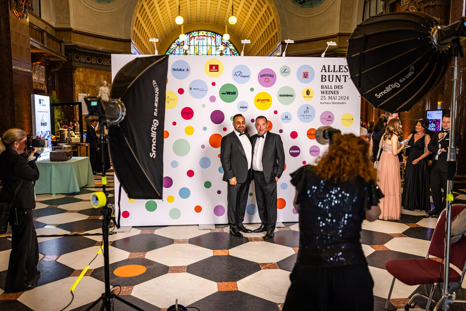 Two men take a photo in front of a photo wall