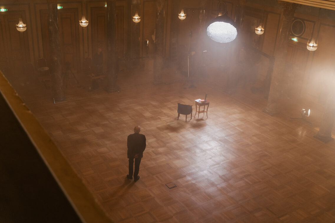 Exception from above. A man is standing on the left, while a table and a chair are further away on the right.