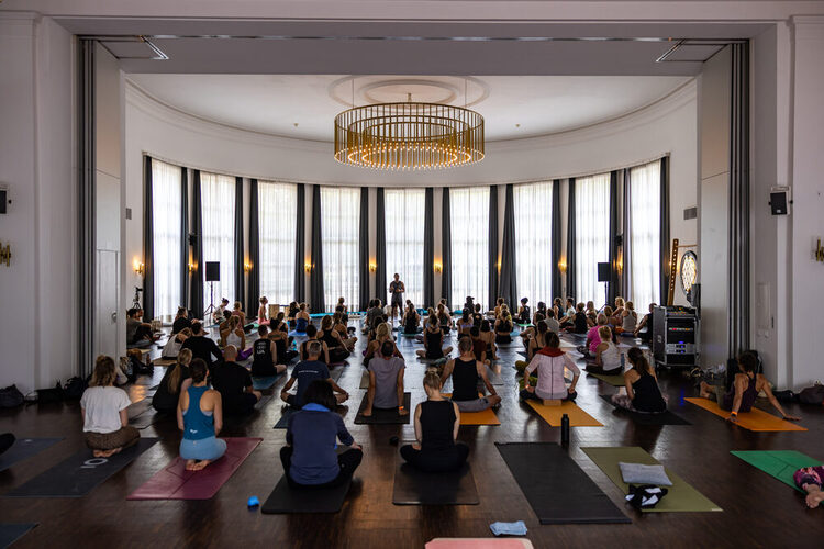 Veranstaltungsgäste sitzen auf den Yogamatten und hören den Vortrag zu.