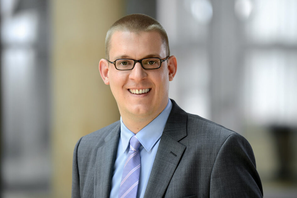 Porträtfoto Sebastian Dietrich lächelnd mit Kurzhaarfrisur und schlichter Brille mit Hemd, Sakko und Krawatte.