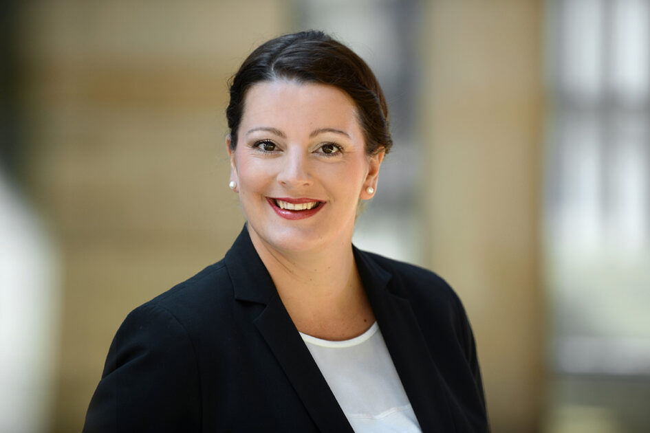 Porträtfoto Ramona Eytzinger mit zurückgebundenen Haaren und Perlenohrringen im Blazer.