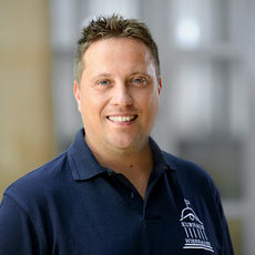 Porträtfoto Michael Hirschochs lächelnd mit Kurzhaarfrisur. Er trägt ein Poloshirt mit dem Kurhaus-Logo auf der linken Brust.