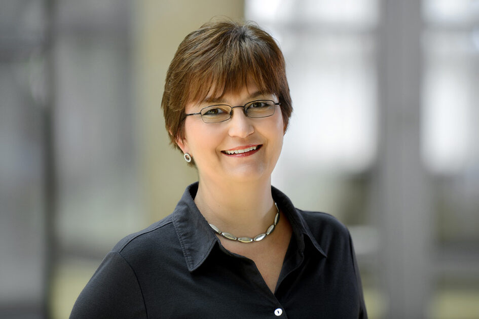 Porträtfoto Stefanie Stüber mit Kurzhaarfrisur und Pony, die eine klassische schwarze Brille, schlichte Ohrringe und Kette trägt.